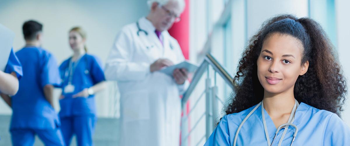 medical student looking directly into camera. Other healthcare providers in background