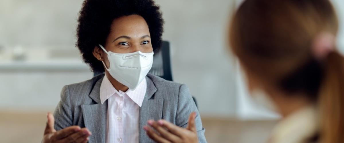 Black woman in a N95 mask talking to another person