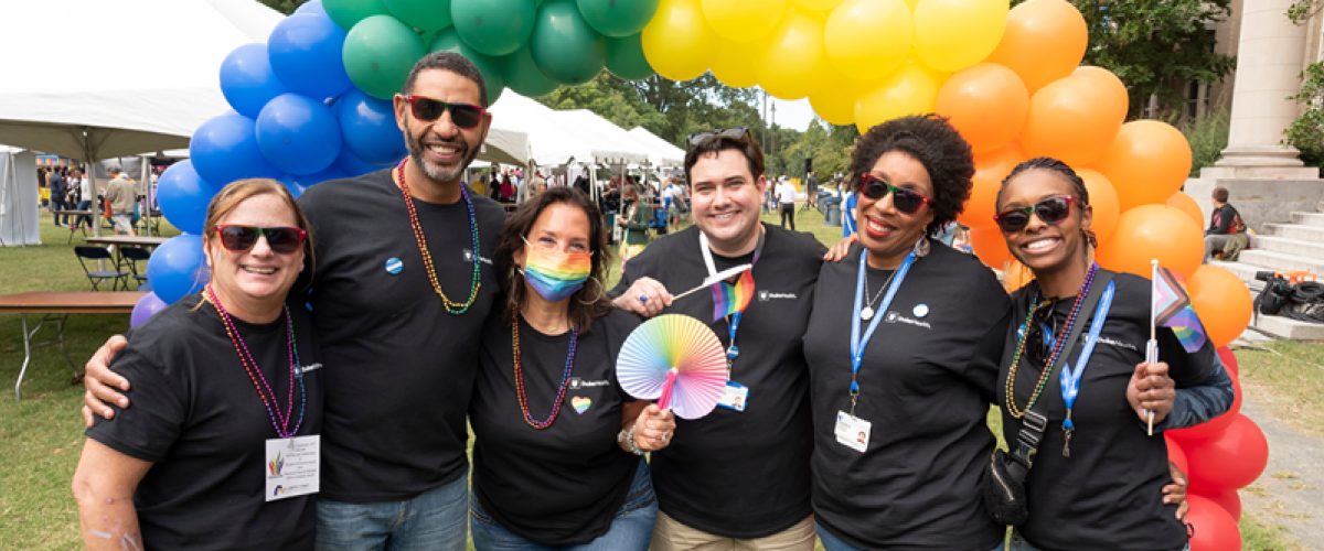The office of EDI at pride in matching t-shirts under a balloon rainbow 