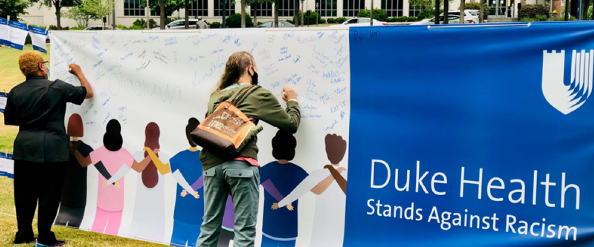 two people signing a banner that says "Duke Health Stands Against Racism