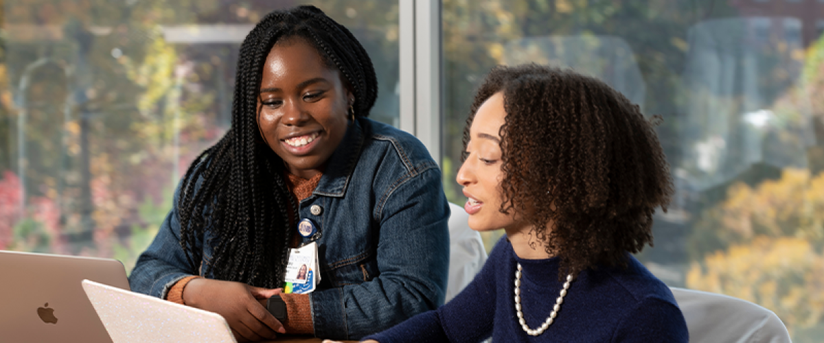 two black women sitting at a table looking at a laptop