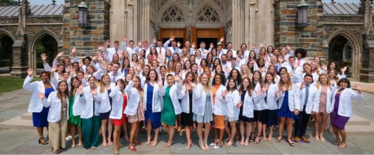 A group of students in white coats outside the Duke Chapel