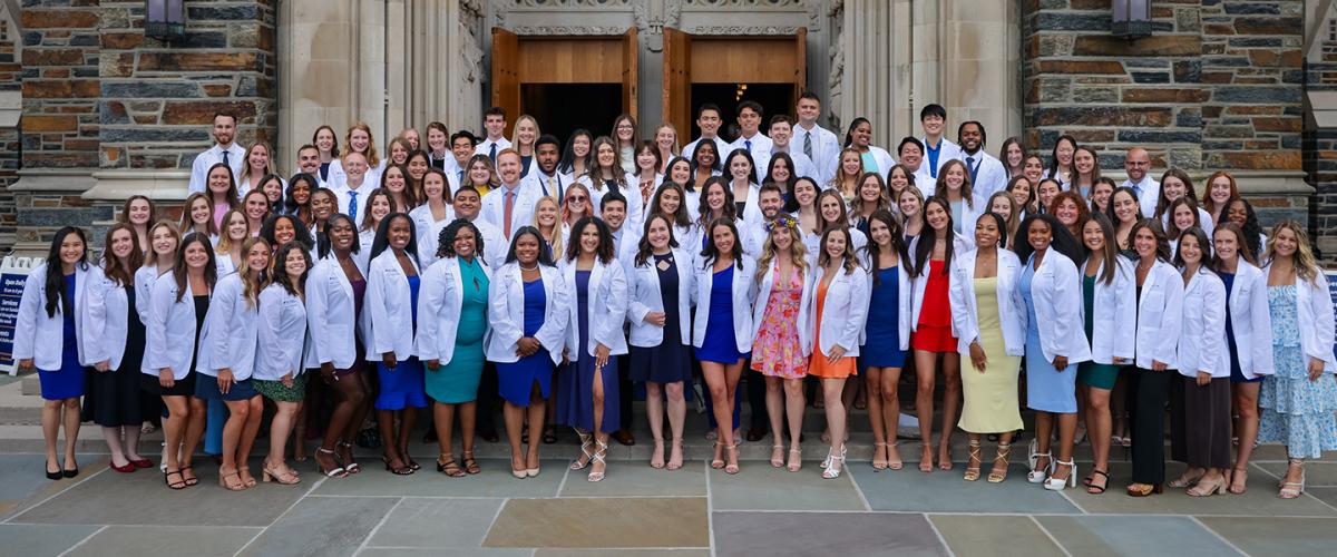 more than 100 students in white coats posing in front of Duke Chapel