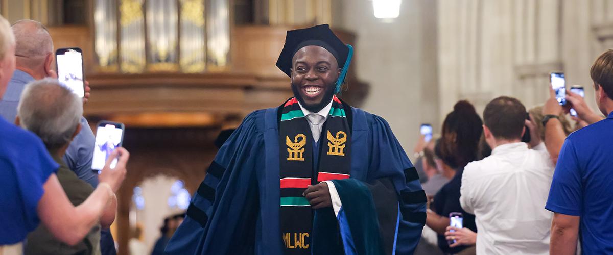 a student in graduation cap and gown smiling as he walks down an aisle at Duke Chapel