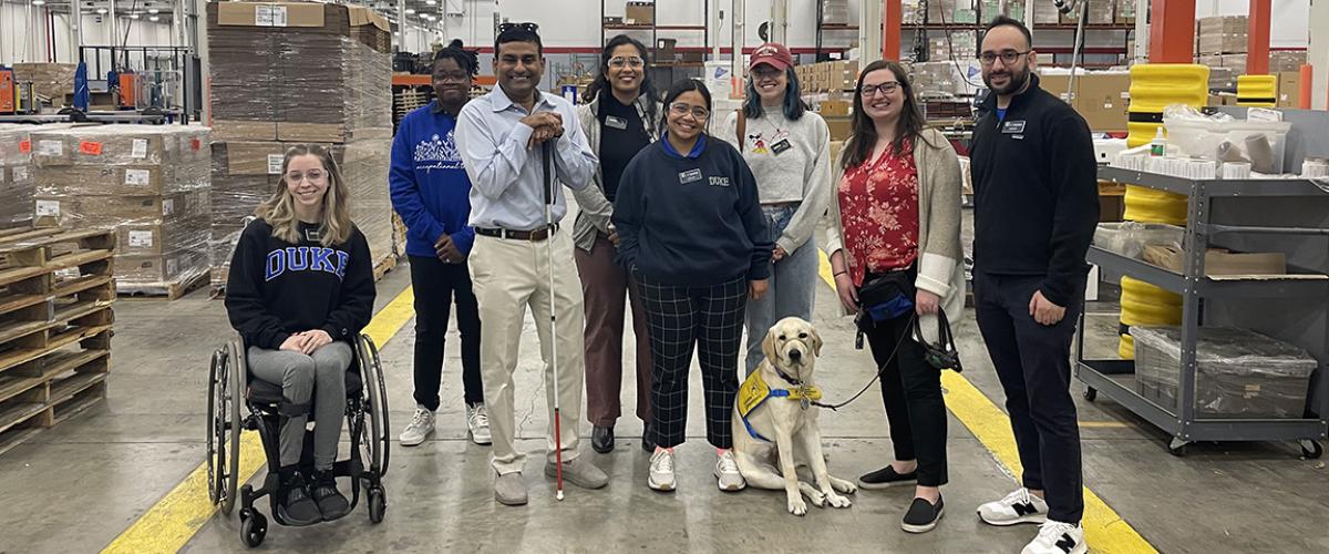 students, faculty and others and a service dog standing in a warehouse