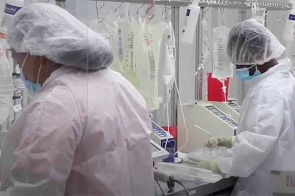 back of two healthcare workers in PPE, preparing infusion bags, with ready bags hanging in front of them.