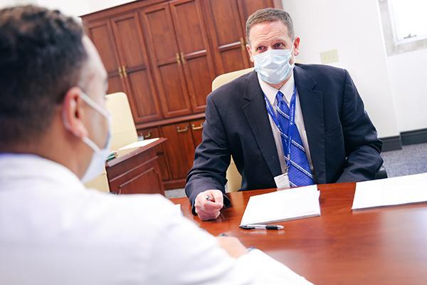 A masked Dr. Grant meeting with a colleague across a table