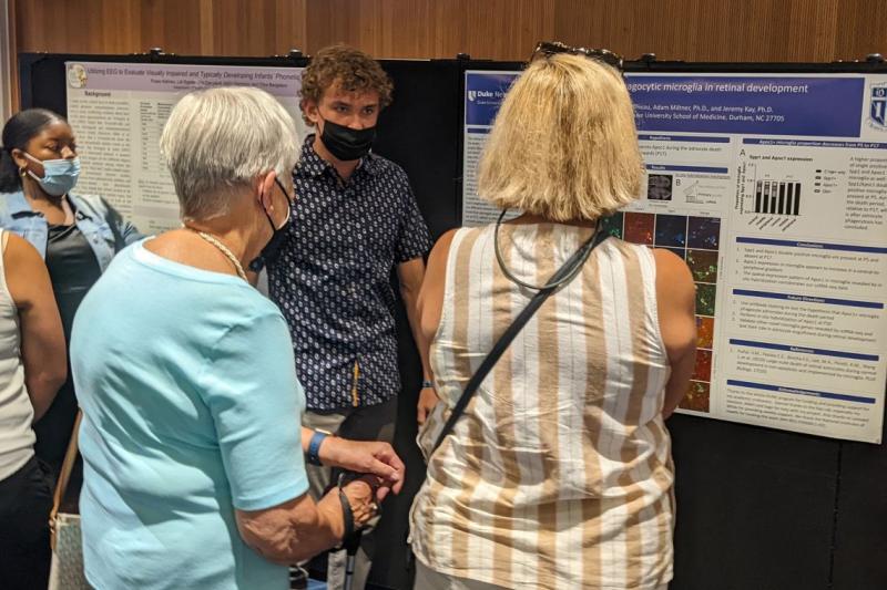 student speaks with people at poster presentation