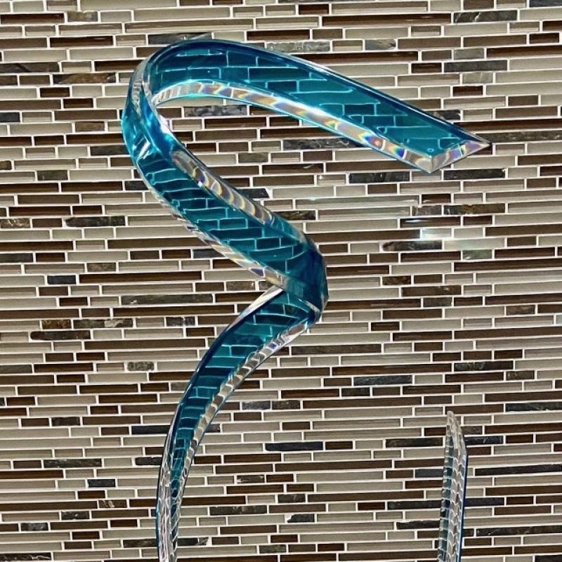Glass sculpture of a teal ribbon against a glass tiled background