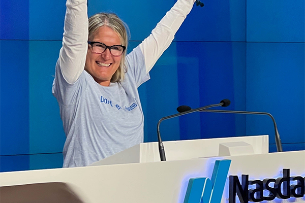 Woman with hands raised in celebration behind a NasDac podium