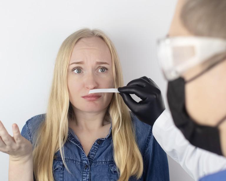 Blond woman looking confused sniffing a test strup held by a masked and gloved healthcare worker