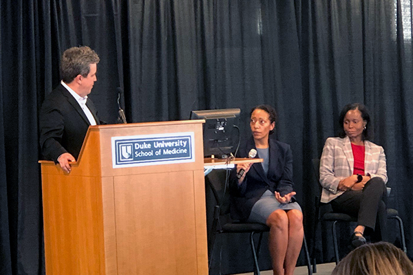 Dr. Hernandez at a podium speaking with Drs. McElroy and Johnson