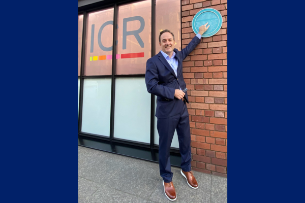 Simon Gregory stands and points at plaque outside of the Institute of Cancer Research in London