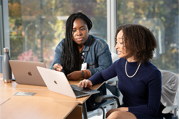 Two Black women med students sitting at a table looking at their computers. 