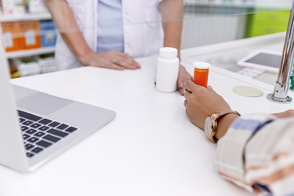 The brown hands of two people passing medication across a pharmacy counter