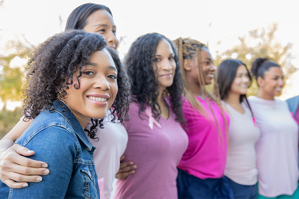 Black and Brown women with their arms around each other - the closest one looking directly at the viewer