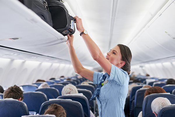 flight attendant pulling a bag down from an overhead bin