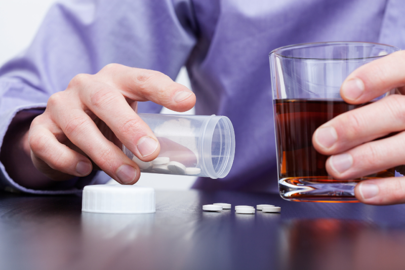 Person dispensing pills in one hand, with an alcoloholic beverage in the other hand
