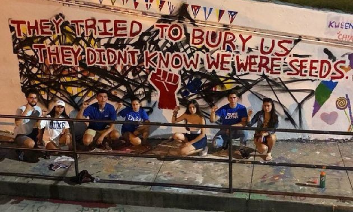 students with fists raised in front of mural