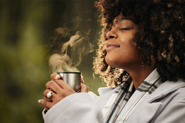 Curly haired Black woman enjoying the scent from a steaming mug.
