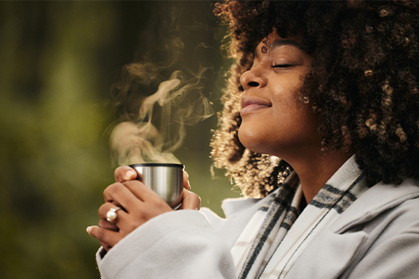 Curly haired Black woman enjoying the scent from a steaming mug. 