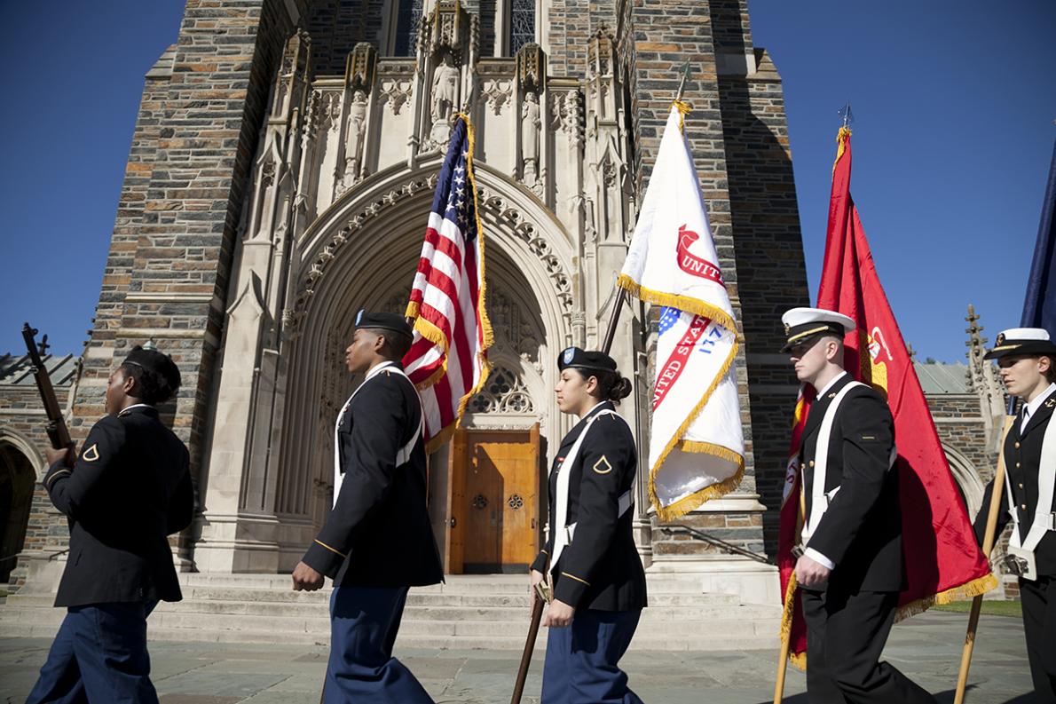 students in military uniforms carry armed service flags in front of Duke Chapel