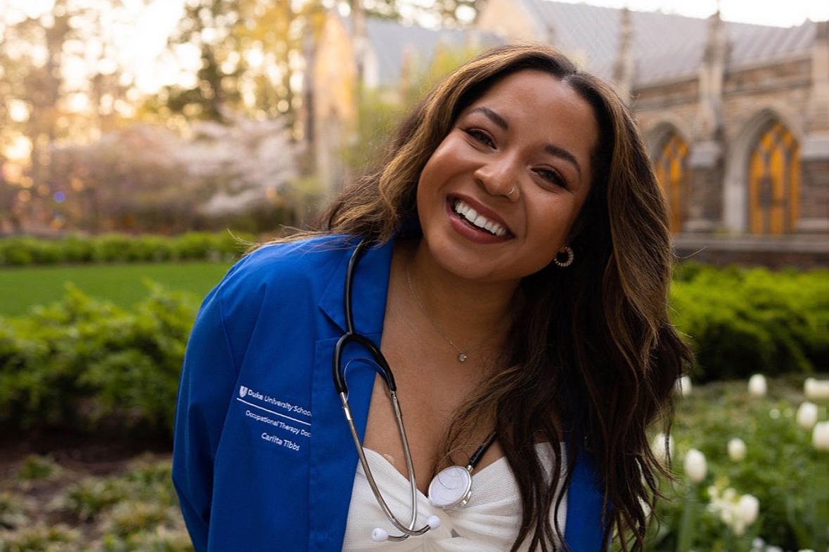 Carlita smiling in her blue OT doctor coat outside Duke Chapel