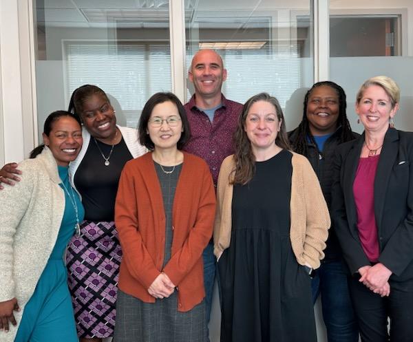 Image: Several colleagues gathered in an office, smiling and interacting, showcasing teamwork and collaboration.  