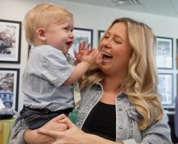 A woman smiles at a young boy she's holding as he laughs and claps his hands