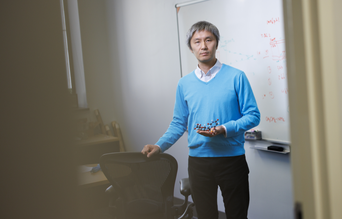 Ken Yokoyama standing in front of a whiteboard holding a model of a molecule