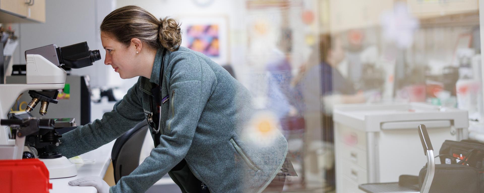 physician looking into a microscope in a lab