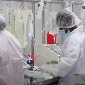 back of two healthcare workers in PPE, preparing infusion bags, with ready bags hanging in front of them.
