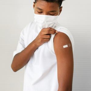 masked student pulling up his sleeve to show a band aid on his arm 