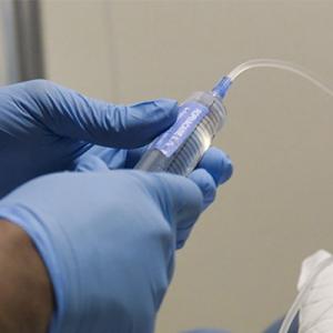 blue gloved hands holding a syringe with a tube coming from the end. 