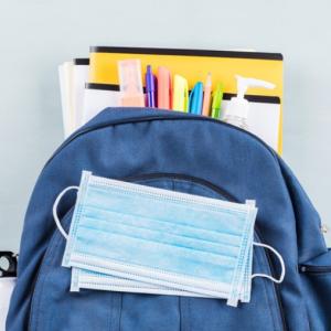 backpack with school supplies hanging out of it and a blue paper mask on top. 
