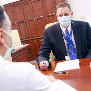 A masked Dr. Grant meeting with a colleague across a table