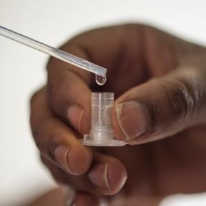 Hand of a Black person holding a small vial for lead testing 