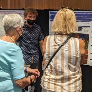 student speaks with people at poster presentation