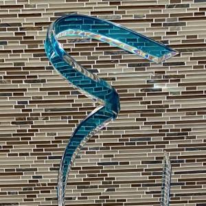 Glass sculpture of a teal ribbon against a glass tiled background