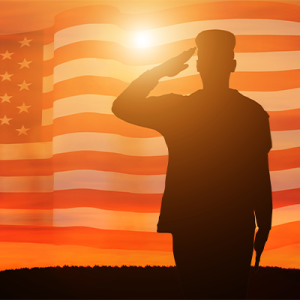 Silhouette of soldier saluting a flag waving in the sky at sunset
