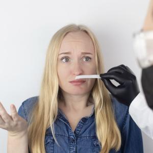 Blond woman looking confused sniffing a test strup held by a masked and gloved healthcare worker