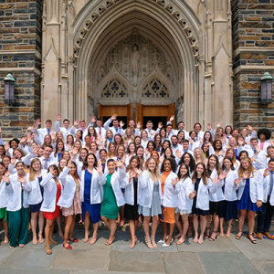A group of students in white coats standing in front of the Duke Chapel