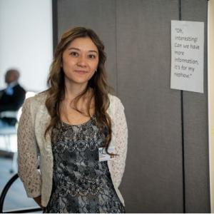 A dark haired young lady standing in front of a poster