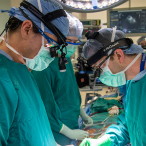Three surgeons in the OR, masked and gowned, performing a heart transplant