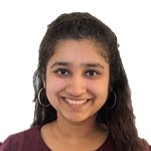 Headshot of Nishma Chakraborty wearing marroon scoop neck shirt, hoop earrings, with curly hair half up