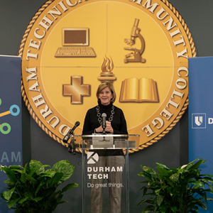 Mary Klotman, MD at a podium in front of the Durham Tech school seal.