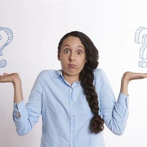 Photo of a woman holding up two question marks while shrugging her shoulders