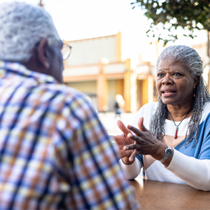 Black older couple talking together across a table outside. 