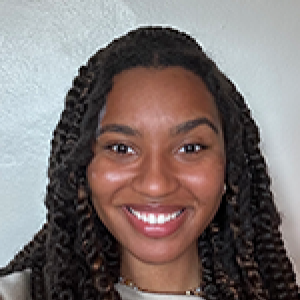 Headshot of Abra Granger smiling at camera in front of white backdrop with dark hair falling in front of shoulders over cream sweatshirt