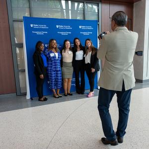 five students posing for a photo in the background with a photographer in the foreground